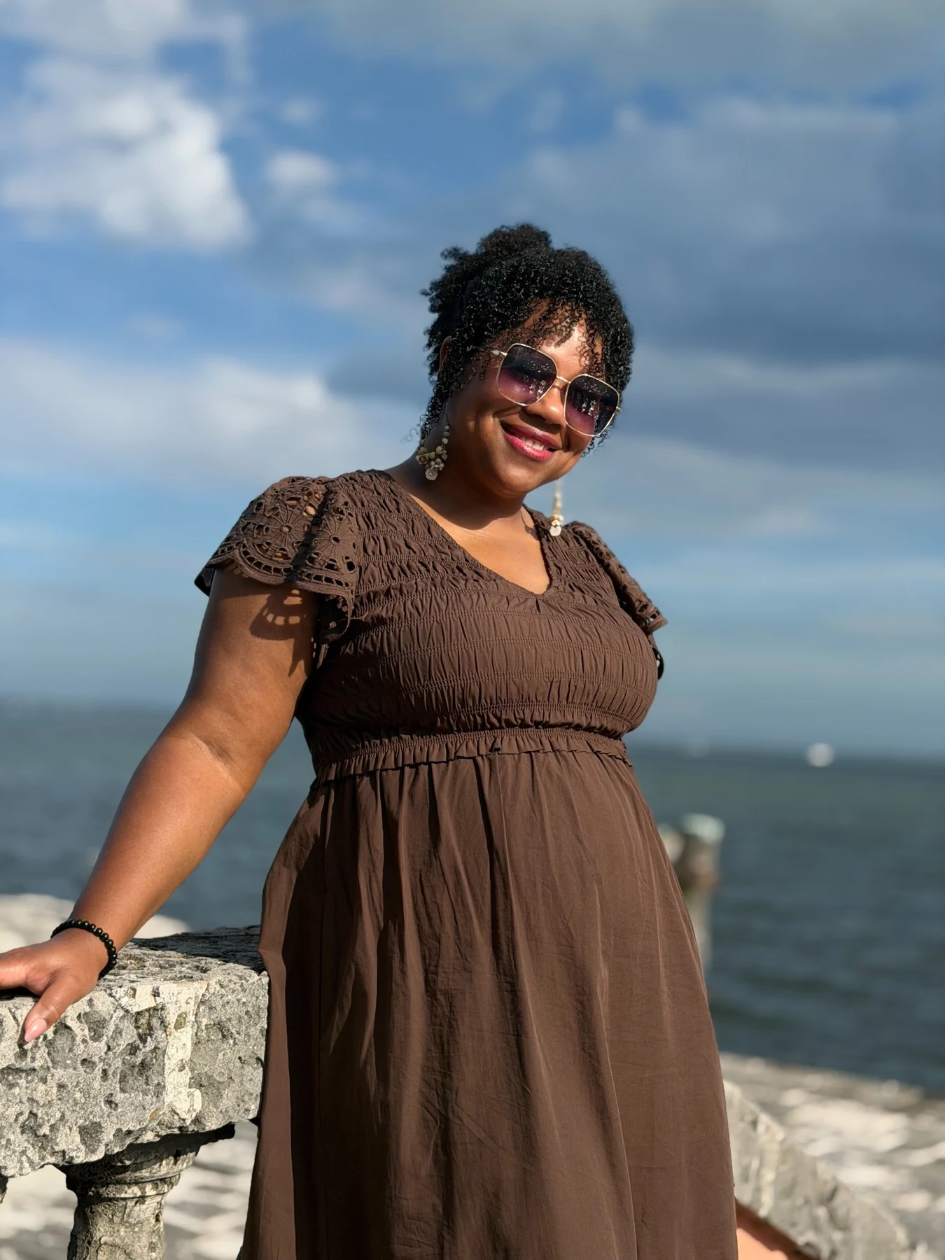 Shay smiling in a brown dress beside the waterfront